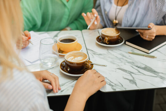 Three young women discussing work processes, signing documents and drinking coffee at a cafe