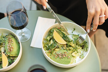 Overhead view of a woman eating a green salad with avocado, cucumber and toasted sunflower seeds