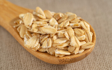 Rolled oats on a wooden spoon over a beige textured background. Perfect for healthy eating and organic food themes.
