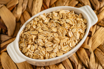 Rolled oats in a white ceramic dish placed on a rustic woven background. Perfect for healthy and natural food themes.