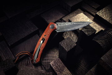A beautiful folding knife with a wooden handle and a Damascus steel blade on a beautiful background