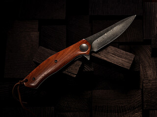A beautiful folding knife with a wooden handle and a Damascus steel blade on a dark background