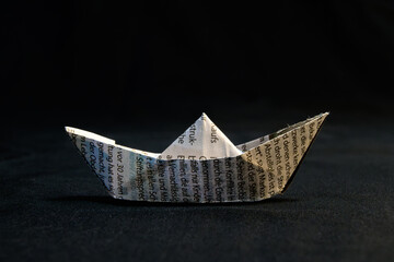 Obraz premium Simple Origami Boat Made From Newspaper On Dark Background