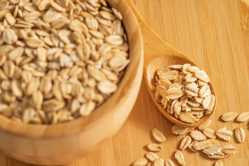 Cuenco y cuchara de madera llenos de hojuelas de avena sobre una superficie de bambú, ideal para conceptos de comida saludable.