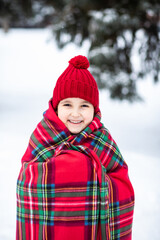 Happy little smiling girl in red cap and checkered plaid standing near by spruce. Holiday celebrate concept.