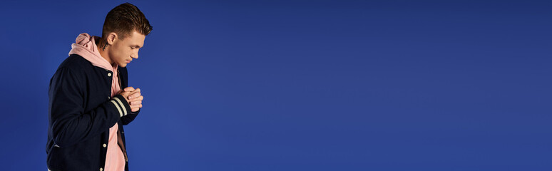 Young man stands in deep thought against a solid blue background.