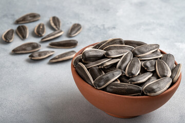 Black sunflower seeds in a bowl on light background