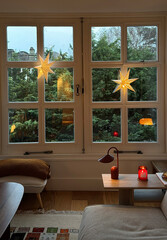 Cozy living room with lights on a windy rainy day against window with green tree background.