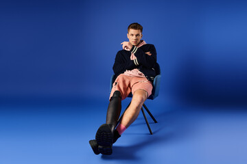 A young man in a prosthetic leg sits stylishly in a modern setting.