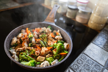 Top view of the frying pan with fresh vegetables and chicken on an induction stove in the home kitchen. Food for meat eaters. Homemade food. Nutrition and a healthy lifestyle. Culinary at home. 