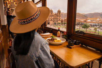 Latin tourist having lunch and looking at the Cusco square from the window