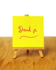 A yellow thank you note with the words 'Dank je,' meaning 'thank you' in Dutch, on a miniature easel.