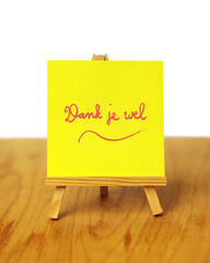A handwritten yellow thank you note with the words 'Dank je wel,' meaning 'thank you' in Dutch, on a miniature easel.