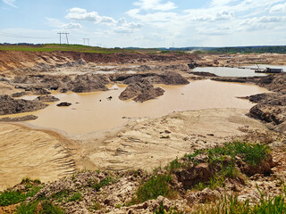 Large excavation area features muddy water pools and rocky terrain under a bright sky in a rural...