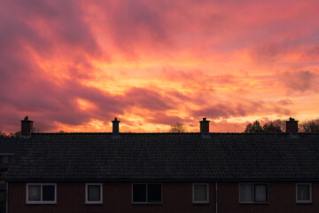At sunset, rooftops of houses in a 1950s Dutch neighborhood, with clouds and black roof tiles.