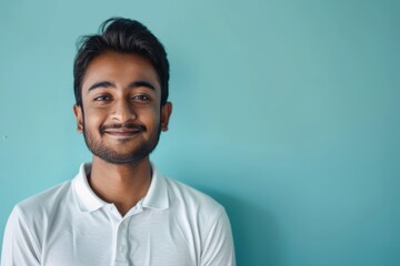 Fototapeta premium Portrait of a blissful indian man in his 20s donning a classy polo shirt isolated on soft blue background