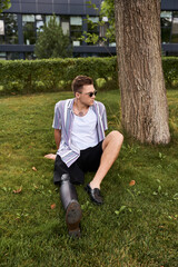 A young man with a prosthetic leg sits on the grass, enjoying the weather in a park.