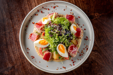 A beautifully arranged salad featuring fresh greens, cherry tomatoes, sliced hard-boiled eggs, and seared tuna garnished with a creamy dressing, on a stylish plate. Perfect for food photography.