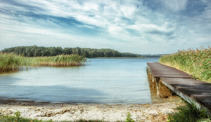 Fototapeta premium Beautiful, deserted beach and jetty in Poland in midsummer. Lonely idyll without people in the great outdoors. Wooden pier on the beach and pier for boats. Fantastic nature in deserted paradiese.