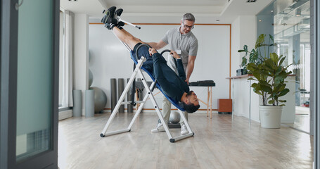 People, inversion table and upside down for physical therapy with support, balance and recovery at...