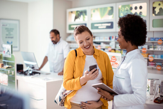 Female pharmacist helping pregnant woman in drug store