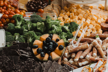 Vibrant Grazing Table with Broccoli, Cantaloupe, Blueberries, Cheese Cubes, Prosciutto-Wrapped Appetizers, and Crackers for Elegant Event Catering and Party Inspiration