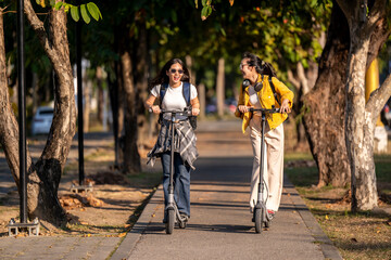 Fototapeta premium Two women riding scooters down a sidewalk
