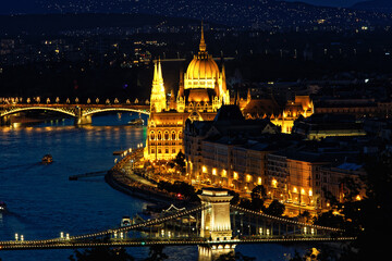 Fototapeta premium Stunning night view of Budapest featuring the illuminated Parliament building, Chain Bridge, and Danube River with reflections and boats. A vibrant cityscape highlighting Hungarian landmarks and archi