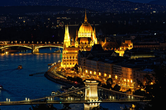 Stunning night view of Budapest featuring the illuminated Parliament building, Chain Bridge, and Danube River with reflections and boats. A vibrant cityscape highlighting Hungarian landmarks and archi - Powered by Adobe