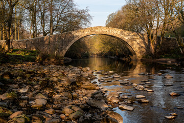Small stone built packhorse bridge over river in sunlight