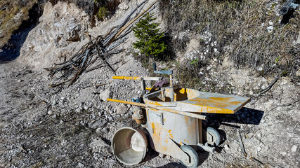 Rustic wheelbarrow and equipment in rocky terrain symbolizing construction challenges and...