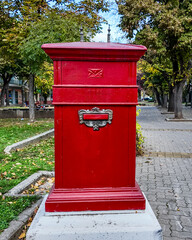 A vintage red postbox in a serene park setting symbolizes traditional communication and mail delivery nostalgia, ideal for illustrating postal services