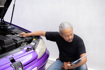 Indonesian male mechanic performing roadworthiness check on car engine, automotive industry concept.