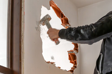 Construction worker demolishing interior brick wall with sledgehammer during renovation
