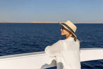 Elegant sexy woman in white dress standing near railings and looking on sunset. Like yacht style.