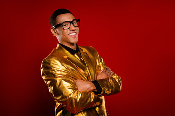 Charming young man in a glossy golden suit stands confidently against a vibrant red background