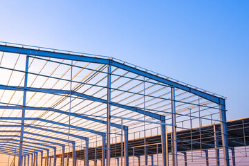 Factory building framework with metal post and roof beam structure  in construction site against evening sky background, low angle view