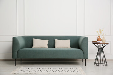Stylish sofa, pillows and side table with decor near white wall indoors