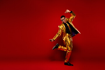 Charismatic young man in a glossy golden suit dancing joyfully against a vibrant red background