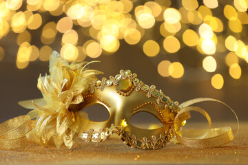 Beautiful carnival mask on golden shiny surface against blurred lights, closeup