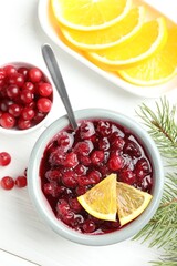 Tasty cranberry sauce in bowl, berries, orange and fir tree branches on white wooden table, top view