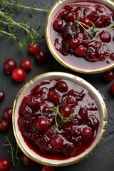 Tasty cranberry sauce in bowls, berries and thyme on black table, top view