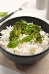 Tasty rice with broccoli and basil in bowl on table, closeup