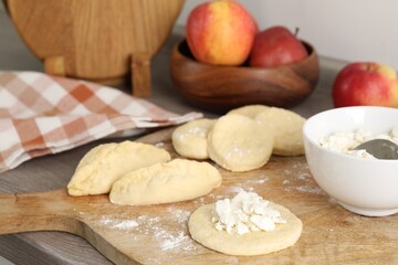 Making pirozhki (stuffed pastry pies). Pieces of dough with cottage cheese on wooden countertop, closeup