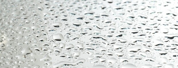 Water drops on light grey glass surface, closeup