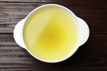 Tasty chicken bouillon in bowl on wooden table, top view