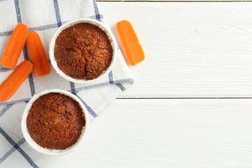 Tasty carrot muffins with fresh vegetables on white wooden table, flat lay. Space for text