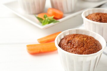 Tasty carrot muffins and fresh vegetables on white wooden table, closeup. Space for text