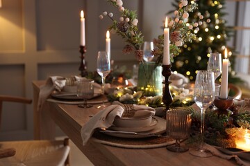 Christmas table setting with stylish dishware, glasses and burning candles in festive decorated room