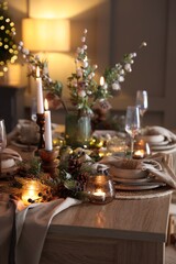 Christmas table setting with stylish dishware, glasses and burning candles in festive decorated room